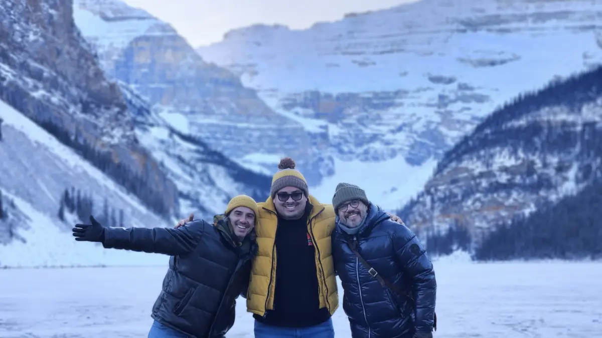Discover Banff on a Premium Day Trip 2 Three people are smiling together in winter clothing, standing on a snow-covered landscape with majestic mountains in the background.